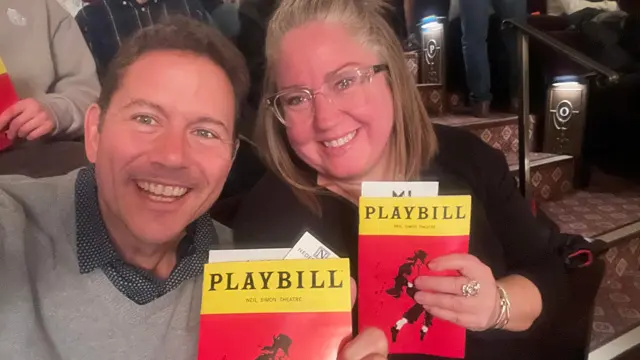 Two people holding a playbill for a show.